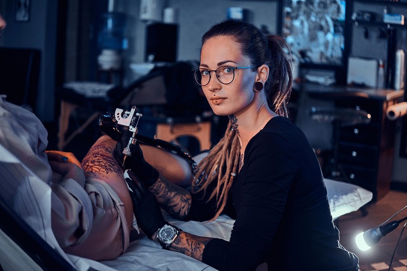 beautiful-young-tattoo-artist-with-glasses-on-doing-a-tattoo-on-a-woman-leg