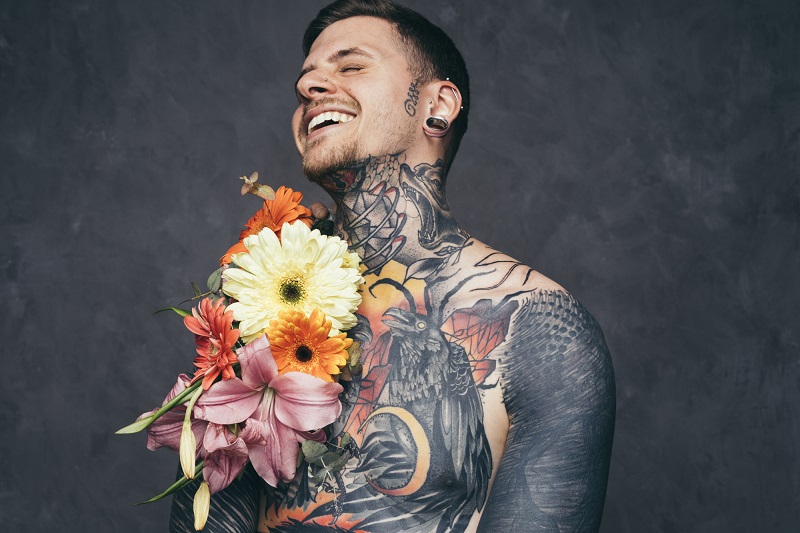 smiling-young-man-with-pierced-ears-with-flowers-and-his-tattooed-body